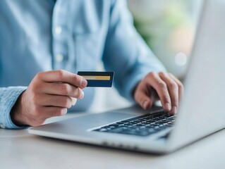 A person making an online payment with a credit card using a laptop in a bright workspace. Focus on finance and technology.