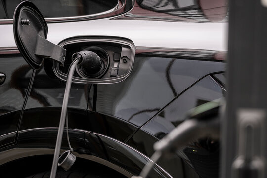 Close-up image showing an electric car being charged with a plug-in charger at a charging station, focusing on the technological and sustainable aspects of modern transportation.