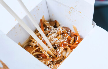 chinese noodle with chopsticks in take away box on wooden table