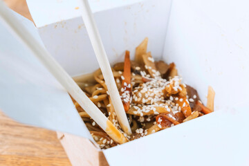 chinese noodle with chopsticks in take away box on wooden table