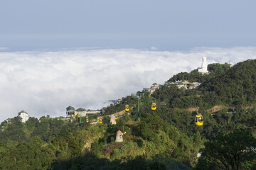 Da Nang, Vietnam - February 10, 2019: High angle view of Bana Hills and Resort with yellow gondola and a statue of the Buddha against sea of clouds on Bana Mountain