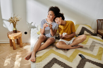 A joyful couple shares laughter while sipping tea on a cozy bed.