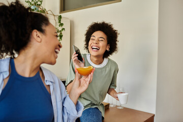 A happy couple shares laughter while sipping coffee and enjoying fruit at home.