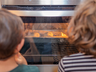 Two children watching baked goods rise in oven