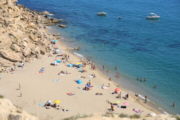 View of La Plagette, a Mediterranean beach bordered by cliffs near Leucate, France featuring golden sands and translucent water with people swimming and sunbathing and boats visible near shore