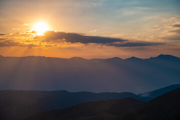 Obraz premium The setting sun over the mountains, the beautiful sun's rays shine through the clouds, the natural background, freedom, tranquility and peace