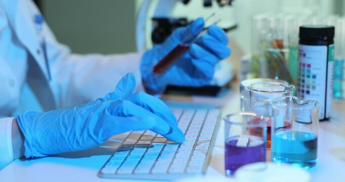 Researcher types on a keyboard while working with test tubes filled with colored solutions