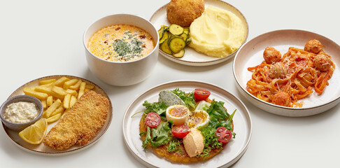 A variety of delicious and appetizing dishes are arranged on a white surface. The dishes include a bowl of creamy soup, a plate of meatballs and pasta, a plate of mashed potatoes