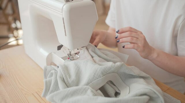 Apparel studio owner sitting at sewing machine and carefully stitching together some material pieces. Working hard on weekday. Sun shining bright. White shirt. Modern technologies.