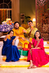 Cheerful Indian couples and friends celebrating Diwali at home with drinks, sweets, taking selfies