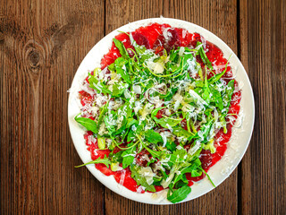 A plate of thinly sliced Carpaccio topped with fresh arugula leaves and parmesan shavings, served...