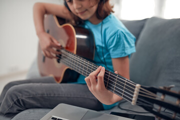 Fototapeta premium Kid playing guitar and watching video lessons on a laptop.