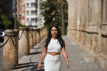 Young, pretty, brunette, Latina woman in a white suit walking down the street like a model. Concept beauty, fashion, trend, city.