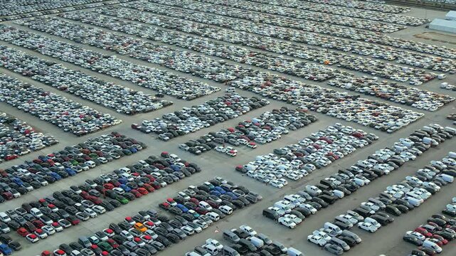 Aerial view of a parking lot filled with cars at a factory or customs warehouse, ready for transport and export. Car manufacturing, importing and exporting cars.