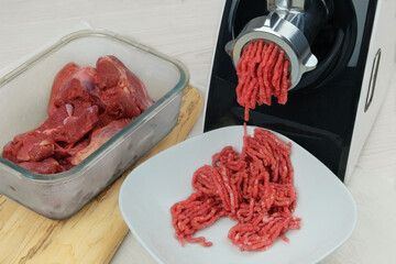 Electric meat grinder with mince meat in bowl in kitchen interior. Homemade minced beef. Cooking at...