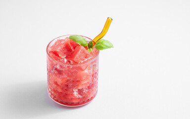 Refreshing watermelon cocktail in glass with basil and ice on a light background.