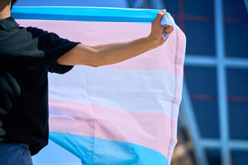 A man holding a transgender flag in front of a building. The flag is large and colorful.