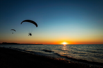 A person is joyfully parasailing high above the ocean during sunset