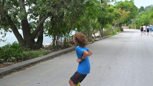 A boy in a blue shirt enjoys hopping on a pogo stick by the seaside, with trees and rocks in the background. The calm sea and distant pier add a peaceful vibe
