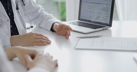 Doctor and a patient. The female physician, wearing a white medical coat over a dark blue dotted blouse, gesturing with his hands during a consultation in the clinic. Medicine concept