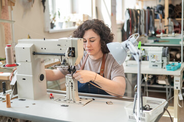 A woman tanner sews a leather belt on a sewing machine. 