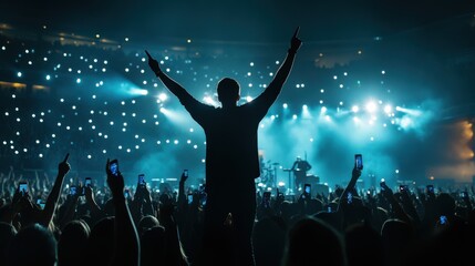 Vocalist in front of crowd on scene in stadium. Bright stage lighting, crowded dance floor. Phone lights at concert. Band blue silhouette crowd. People with cell phone lights