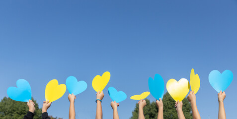 yellow and blue hearts above the head in the hands of children against the blue sky on a sunny day....