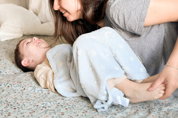 Mom tickles the feet of her little son, wrapped in a blue blanket. Mom and child have fun together...