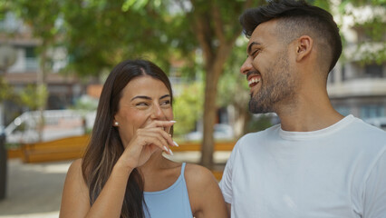 Couple enjoying an outdoor conversation in a city park, man in white shirt, woman laughing, urban setting, smiling, summer day, love, happiness, together in nature