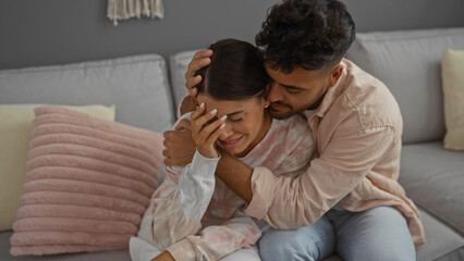 Man comforting woman on a couch in cozy living room, showcasing tender relationship and emotional support in an indoor home environment