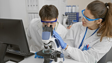 A man and a woman in lab coats using a microscope in a laboratory environment, embodying teamwork in scientific research.