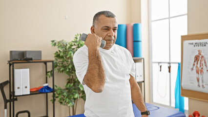 A middle-aged hispanic man exercising with a dumbbell in a rehabilitation clinic's therapy room