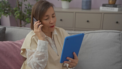 Mature woman multitasking with tablet and phone on cozy sofa indoors