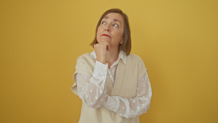 A thoughtful middle-aged woman looks upwards against a yellow background, embodying contemplation...