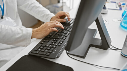 Close-up of a man's hands typing on a keyboard in a modern laboratory setting, indicating...