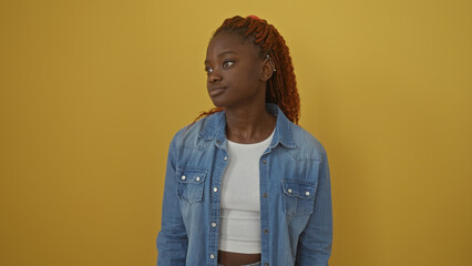 Young african american woman in a denim jacket poses confidently against a vibrant yellow background.