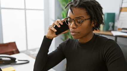 African american woman with dreadlocks wearing glasses using a smartphone in a modern office setting