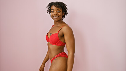 Smiling young black woman in red lingerie posing confidently against a pink background.