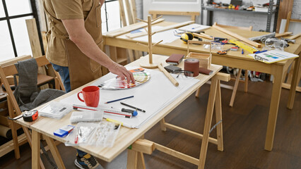 A mature man examines color swatches in a well-equipped woodworking workshop.