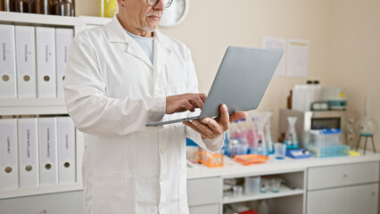 Grey-haired man in lab coat concentrating on a tablet in a modern laboratory setting.