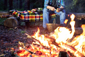 a man sits by the fire in the woods cleaning mushrooms