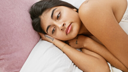 Fototapeta premium Beautiful young indian woman with long hair relaxing in a cozy bedroom setting, exuding serenity and simplicity.