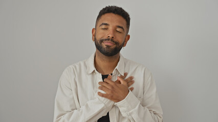 A content young african american man with a beard stands against a white background, grinning with eyes closed.