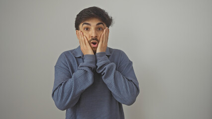 Surprised young man with beard against white background expressing shock with hands on face