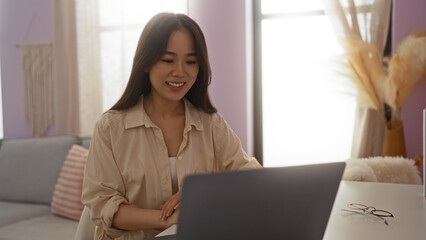 Young chinese woman working on a laptop in a cozy indoor living room environment, showcasing a warm and inviting home setting.