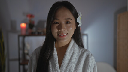 Beautiful young chinese woman in a spa room wearing a white robe and a flower in her hair with a candlelit background creating a calm wellness atmosphere