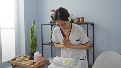 Young chinese woman making a greeting gesture in a serene spa room, surrounded by wellness items and cozy interior details, highlighting the tranquil atmosphere of a beauty salon in china
