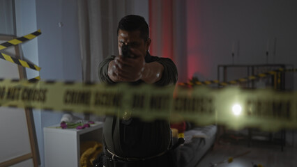 Focused hispanic policeman aiming gun at crime scene inside dimly lit living room