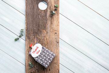 Small black and white gift box, tag with thank you text, laying on a rustic, textured board on a blue and white painted plank background.