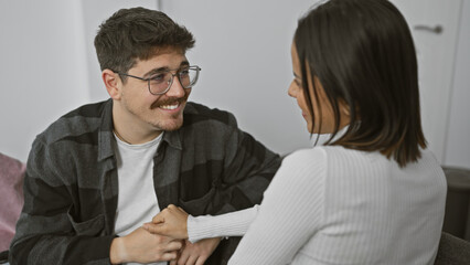 A happy couple, a man and a woman, holding hands in a cozy living room, sharing a moment of tenderness and affection.